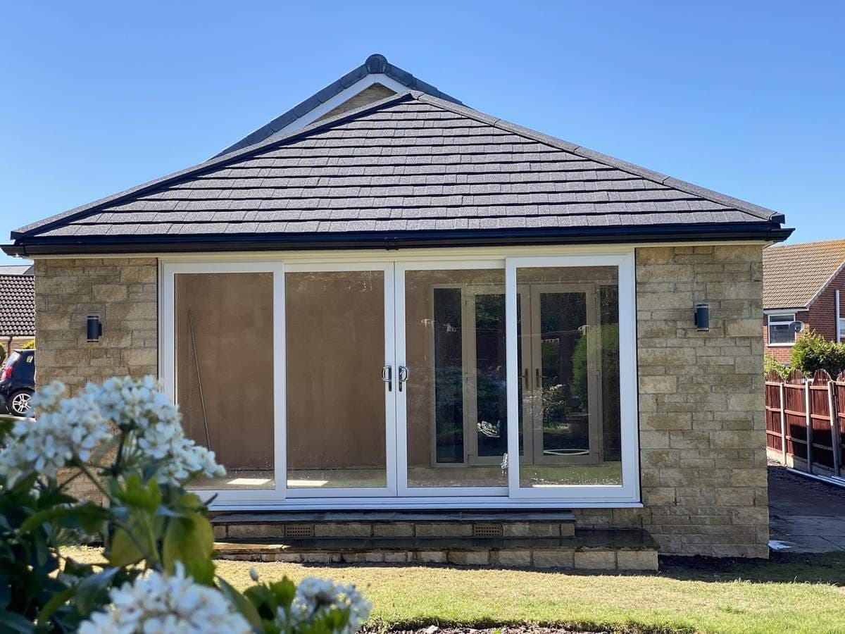A stone garden room with a solid tiled roof, finished in a sunlit garden