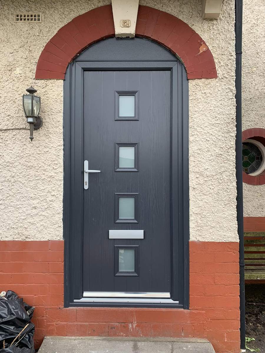 An anthracite composite front door with square glazed panels, under a red brick arch