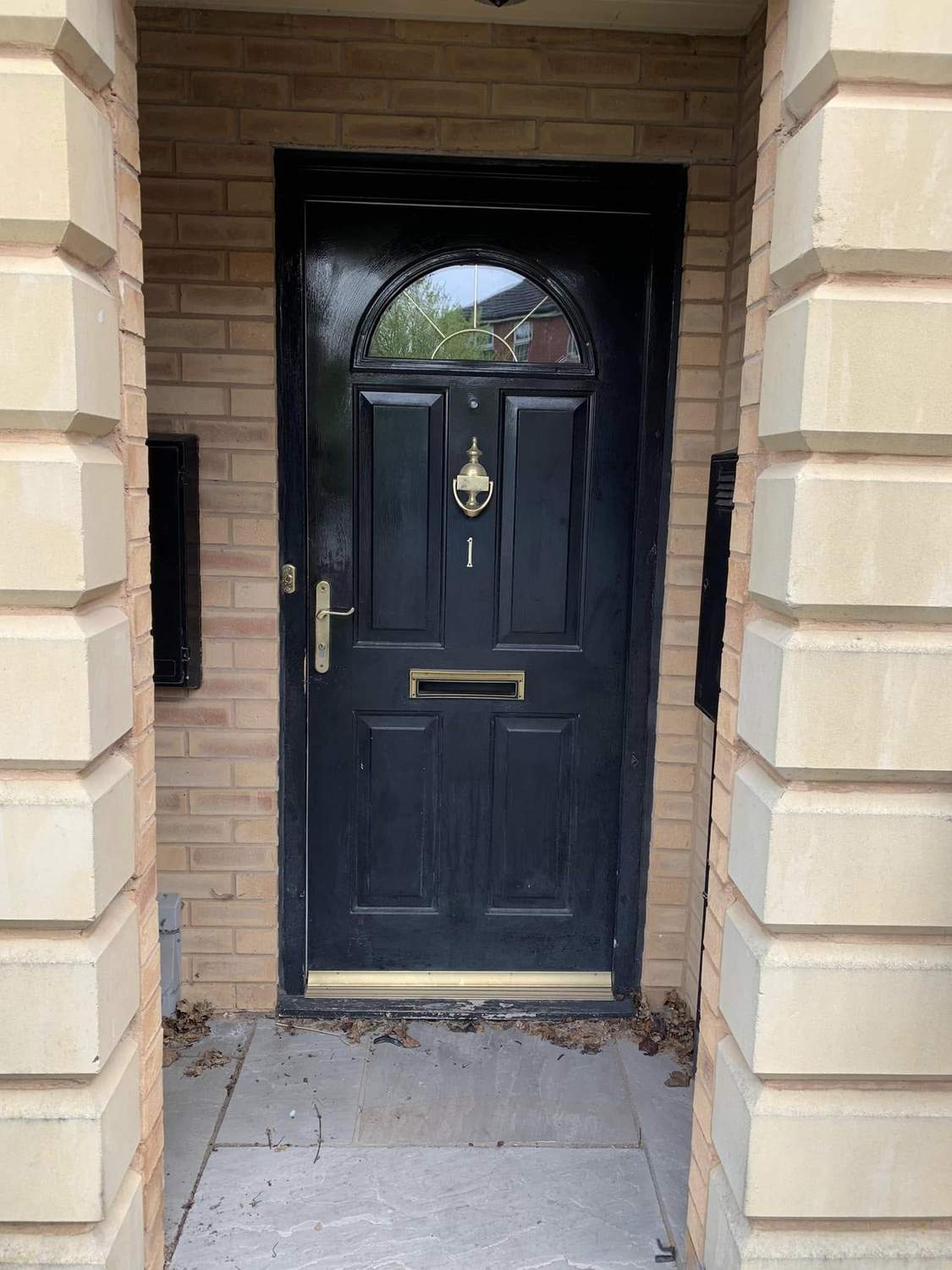 A black composite front door with an arched leaded panel, in a pale stone surround