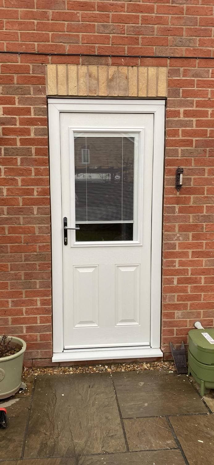 A white composite door with a blind behind the glazed panel, in a red brick opening under a stone lintel
