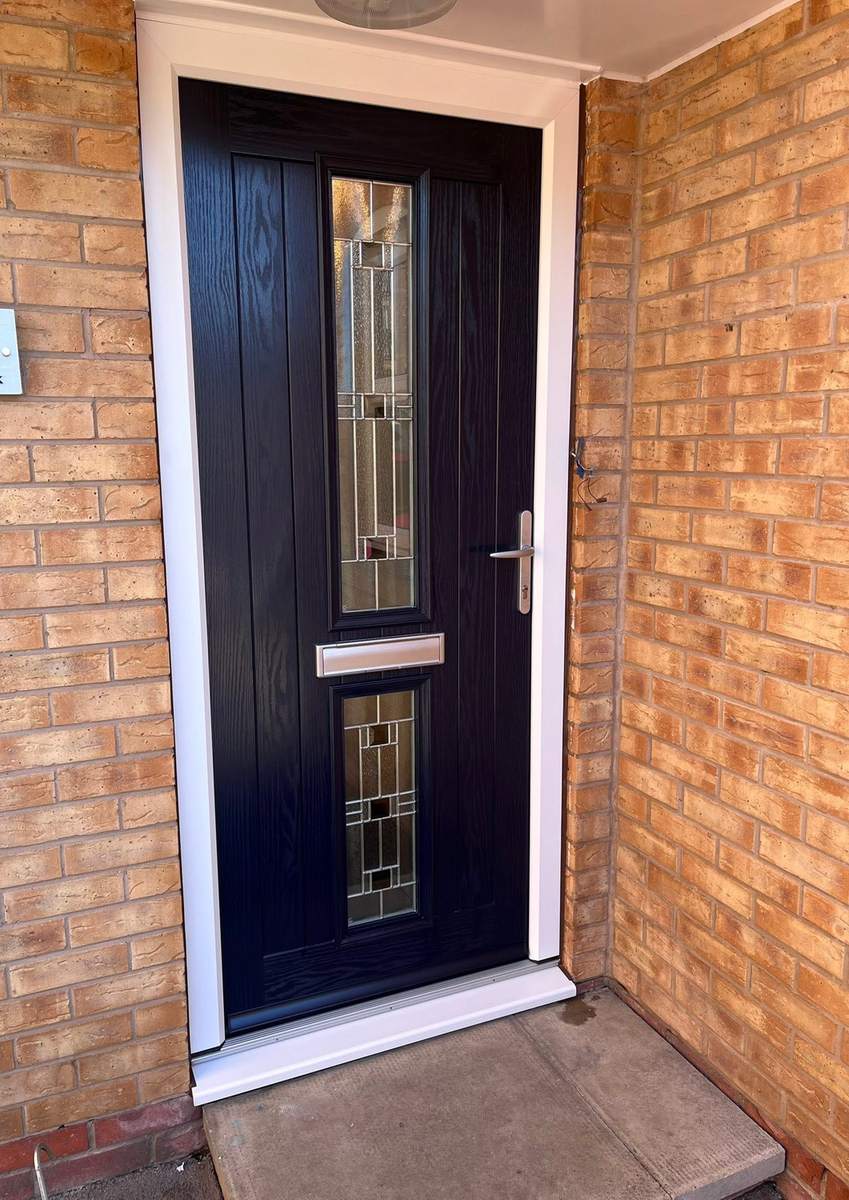 A navy blue composite front door with two leaded glass panels, in a brick porch