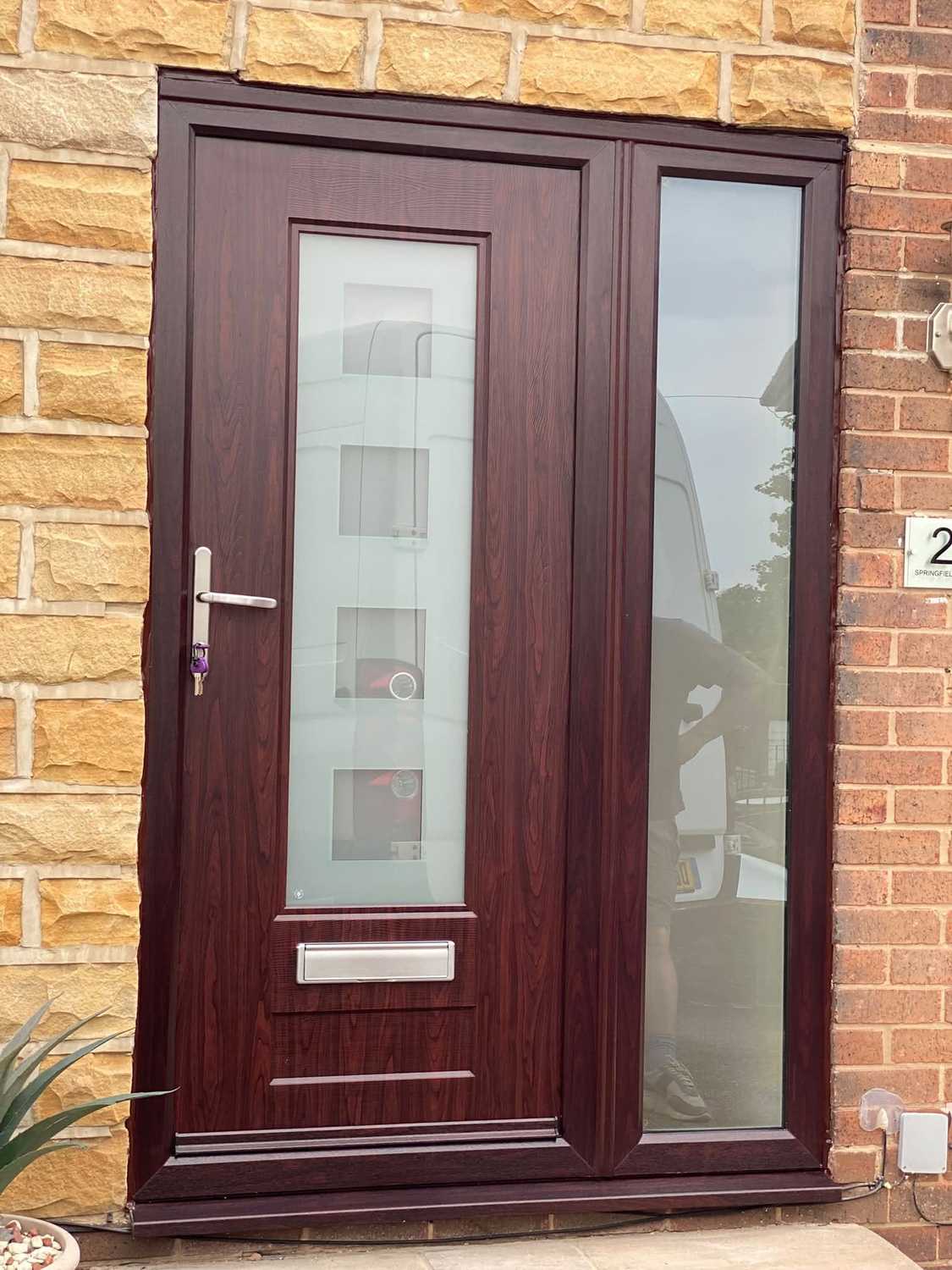 A rosewood composite front door with a glazed side panel, in a stone opening