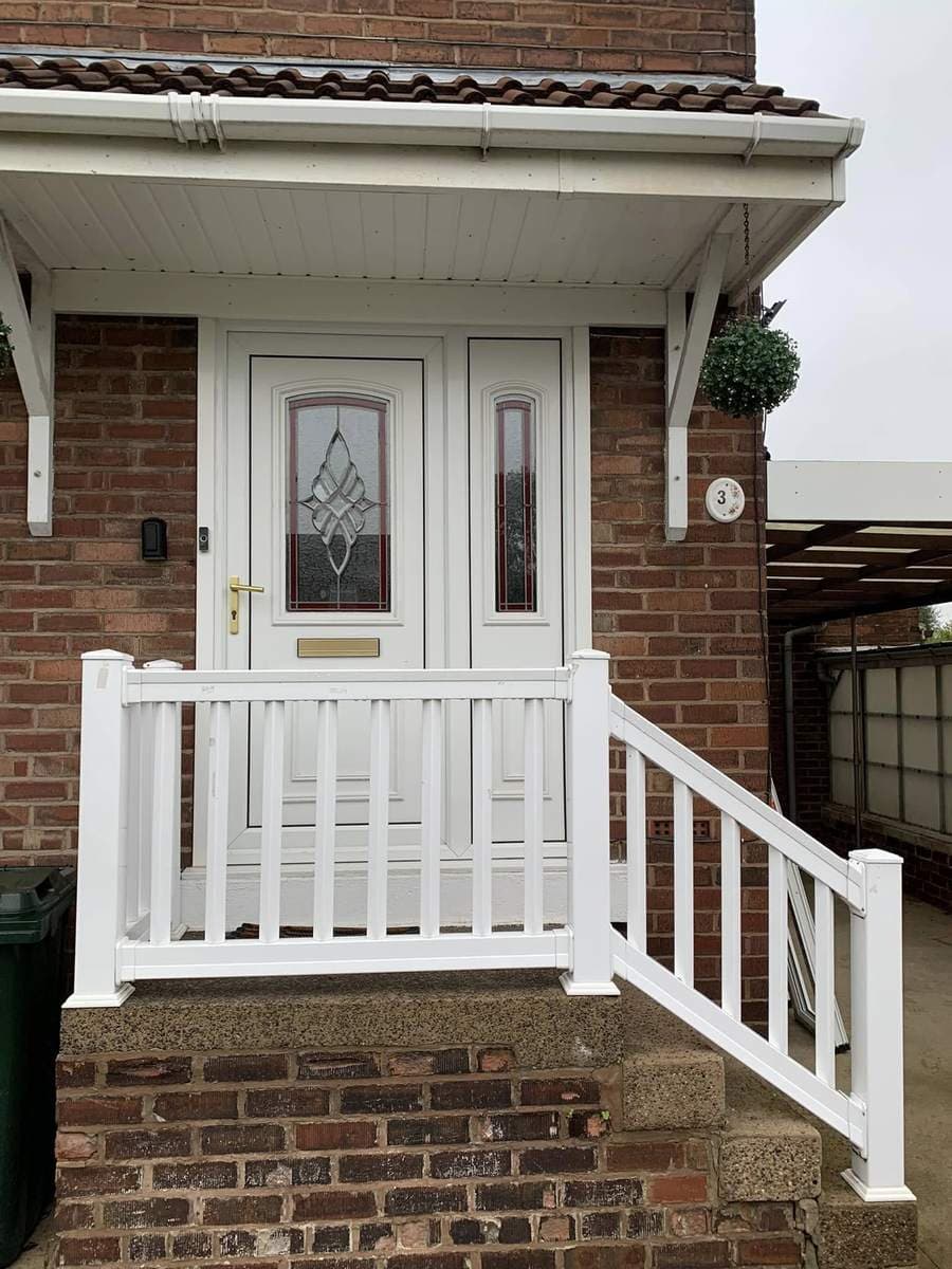 A white composite door in a glazed porch with white railings to the step